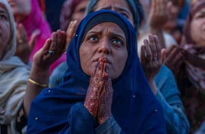 A woman wearing a headscarf, surrounded by others, prays, looking up