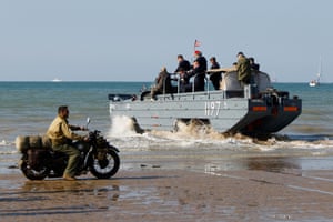 An enthusiast dressed in replica second world war-era military attire on a motorcycle looks on as a DUKW amphibious truck enters the sea at Arromanches-les-Bains, north-west France