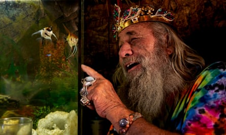 Garth wearing a bright tie-dye T-shirt, a crown and costume jewellery, pointing at fish in a tank