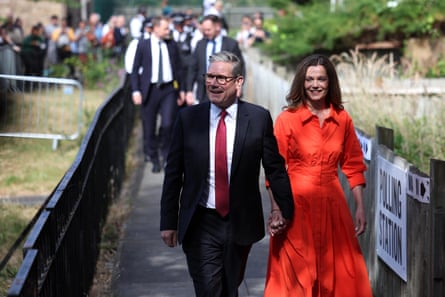Keir and Victoria Starmer walking hand in hand past a sign reading “polling station”