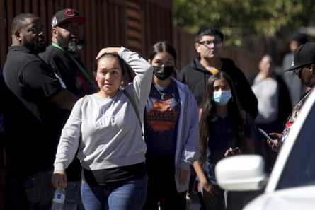 A woman walks down a street with her hand to her head. Two others follow behind her as other people look on nearby.