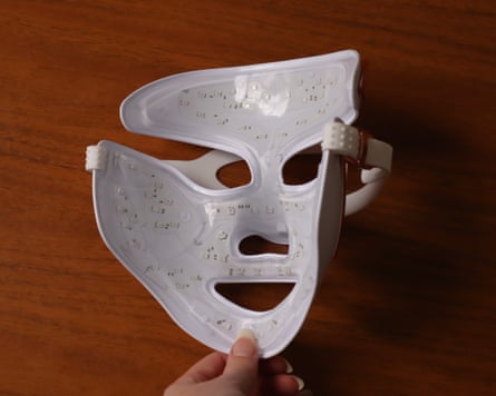 A hand holds open a white LED face mask lined with small lights, on a wooden surface