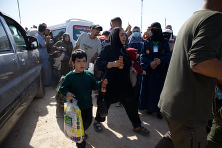 A crowd of Arab families clutching bags with a minibus in the background