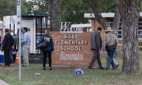 Law enforcement officials stand in front of the sign for Robb elementary school. At the top of the sign is the word 'welcome', at the bottom is the word 'bienvenidos'.
