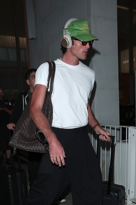 a man in a white T-shirt carrying a large leather bag