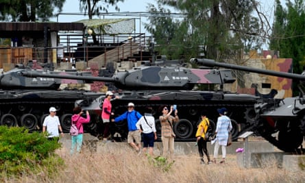 A group of sightseers surround a row of restored tanks in camouflage