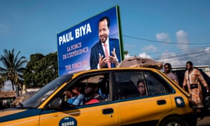 A taxi passes an electoral poster for President Paul Biya