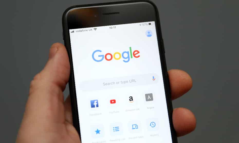A person is seen holding an iPhone showing the app for Google 