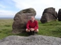 David Clarke crouches beside some standing stones in an open expanse.