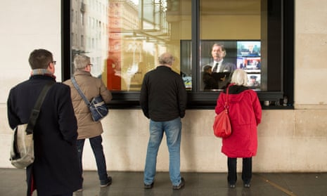 People watch a news report through the windows at BBC Broadcasting House in central London following the death of veteran broadcaster Sir Terry Wogan.