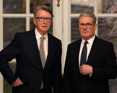 Peter Mandelson and Keir Starmer stand side by side. Both are wearing suits and ties and glasses.