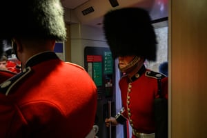 Men in red uniforms and tall bearskin hats board a train