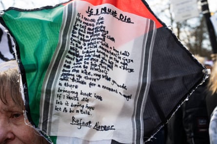 A person holds a Palestinian flag with the words of Refaat Alareer poem If I must die, you must live written in the middle