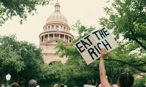 A person holds a sign that says "eat the rich" as they approach a government building