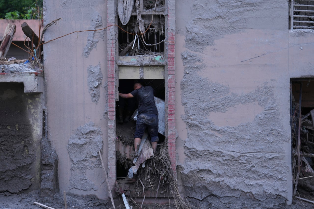 A man stands in an opening of his home, which is filled with debris
