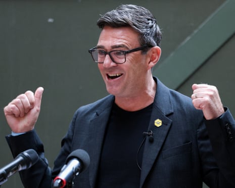 Andy Burnham in front of two microphones, smiling and holding up his hands.