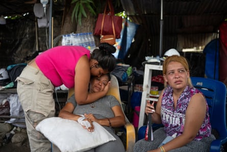 Three women sit in chairs under a shelter looking distraught