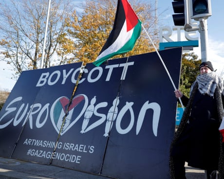 A man waves a Palestinian flag and stands beside a sign that reads: BOYCOTT EUROVISION, ARTWASHING ISRAEL'S GENOCIDE