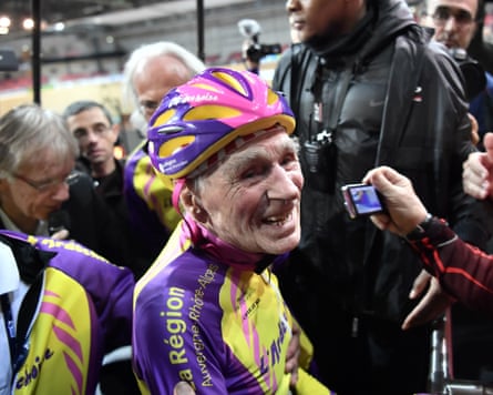 Marchand smiles broadly while wearing cycling equipment, with a crowd of people surrounding him