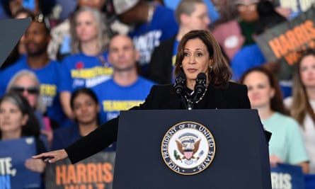 Kamala Harris speaks at a campaign rally: she is at a podium with a crowd behind her, many wearing blue T-shirts and holding Harris/Waltz placards