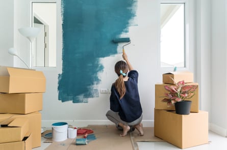 A woman paints an interior wall with paint roller in new house