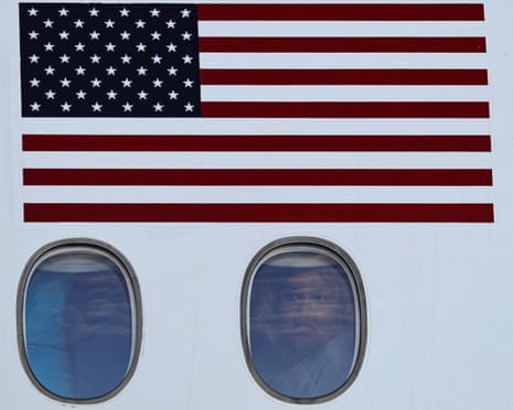 Deported Venezuelan person looking out of airplane window upon arrival in Venezuela. Stars and Stripes flag is on the side of the plane above the window