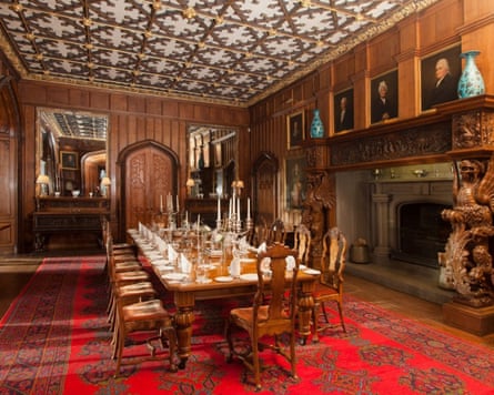 large dining table set for dinner in a panelled room with ornate ceiling and rich red carpet