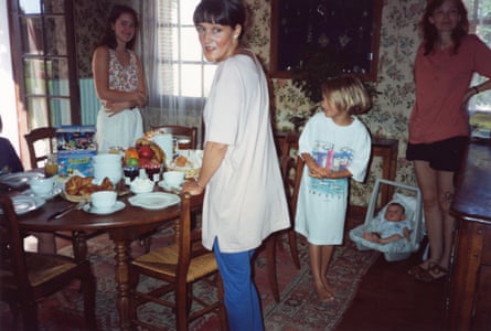 Four women and girls casually stand around a dining table with food on it. The mother is looking directly at the camera.