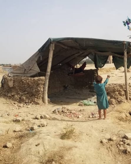 A small child standing beside a small shelter open on three sides with a tarpaulin held up by poles