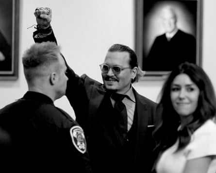 A man wearing glasses and a suit and tie holds a fist up and smiles in court