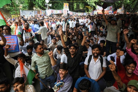 A large crowd of people raise their fists and chant slogans at an outdoor protest with banners overhead