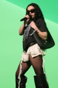 Charli xcx, in sunglasses, a T-shirt, fringed shorts and knee-high boots, sings into a microphone as she clutches a bag under her arm