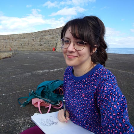 Kat Butler sitting outdoors near the sea, with a sketchpad on her lap