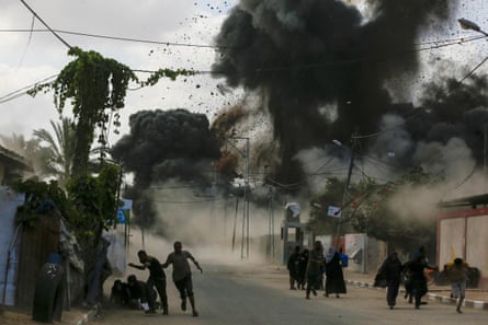 Black bomb clouds and debris fill a street with people running for cover in Deir al Balah, Gaza on 21 August 2025.