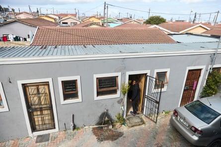A man stands in the doorway of a modest building