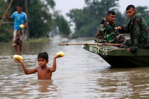 A boy walks away in chest-high floodwater from a soldiers in a boat holding two bags of food above his head