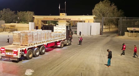People stand around a truck carrying aid, as a gate ahead stands open