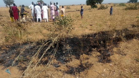 People standing nearing burnt grass after an airstrike