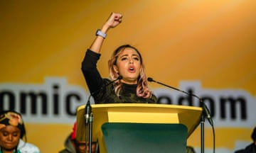 A young Asian woman speaks at a lectern while giving a clenched-fist salute