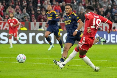 Alphonso Davies shoots to score as an Arsenal defender chases closely