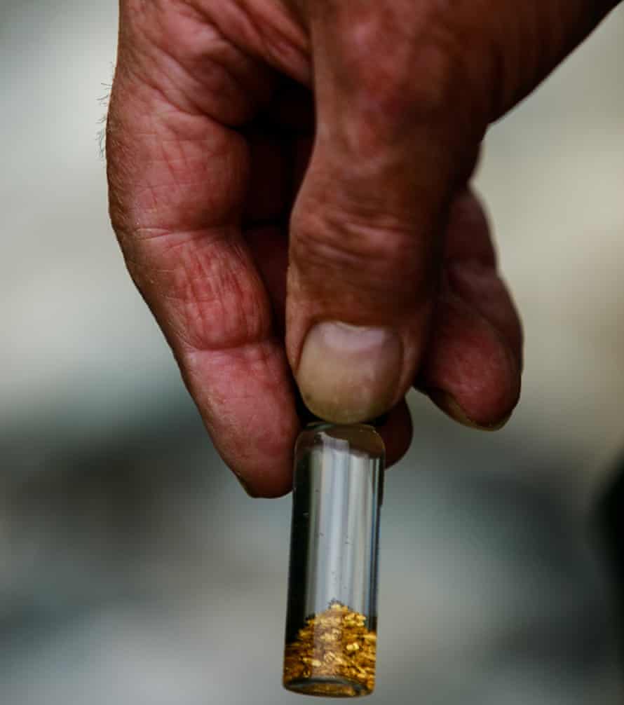 Hand holding tiny jar with panned bits of gold in it