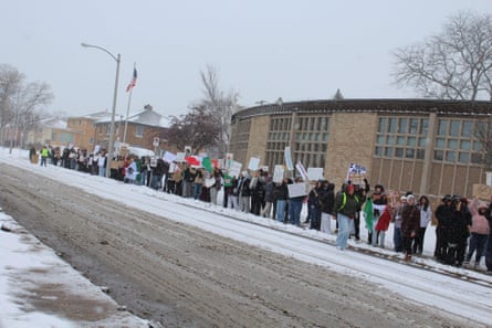 students hold signs outside on a snow-lined street