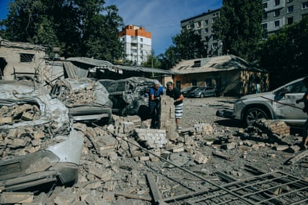 Two people clear debris from around a damaged car