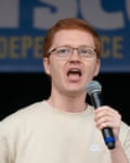Ross Greer speaks into a microphone at a Scottish independence rally in Glasgow, 20 Apr 2024: he is young, with short red hair and glasses, and is wearing a cream-coloured Nike sweatshirt.