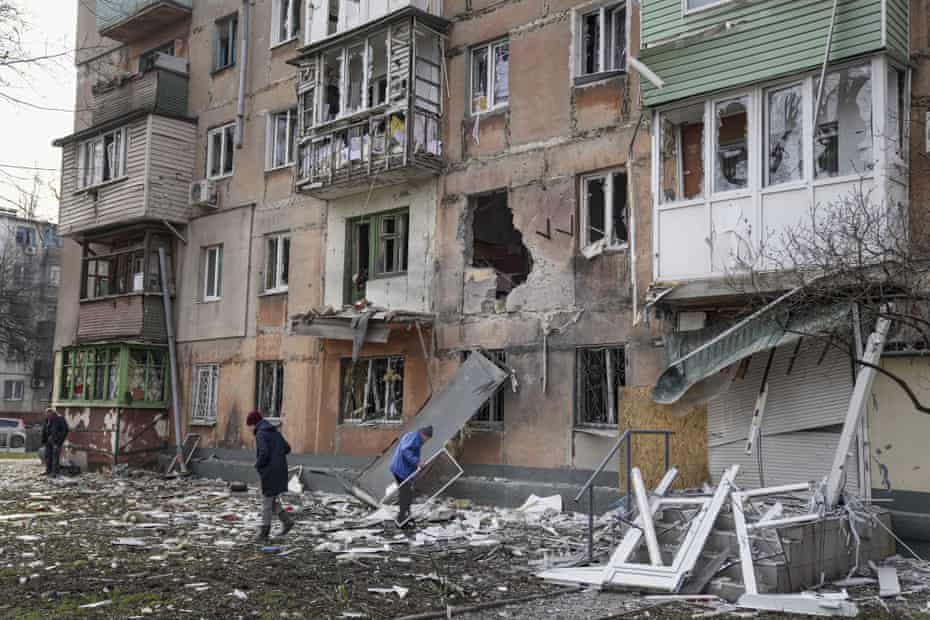 People walk past a destroyed apartment building.