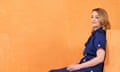 Laura Kuenssberg sitting on orange blocks in an orange space, wearing a navy buttoned long dress and white court shoes