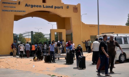 A line of Africans wait at a border point's locked gate with suitcases and bags
