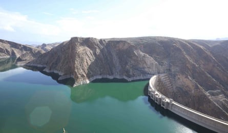 Still green water surrounded by hills and dammed by a high concrete wall.