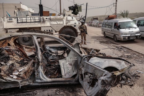 A member of the UN peacekeeping force stands by a burned out car in Qasmiyeh