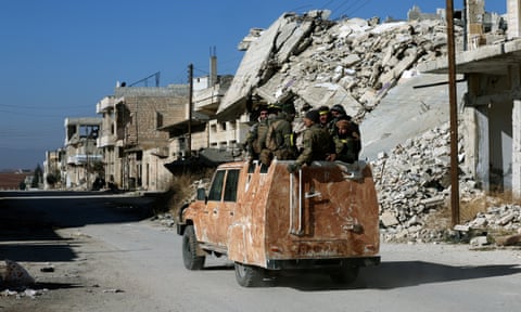 Syrian opposition fighters sit on a vehicle moving past a ruined building